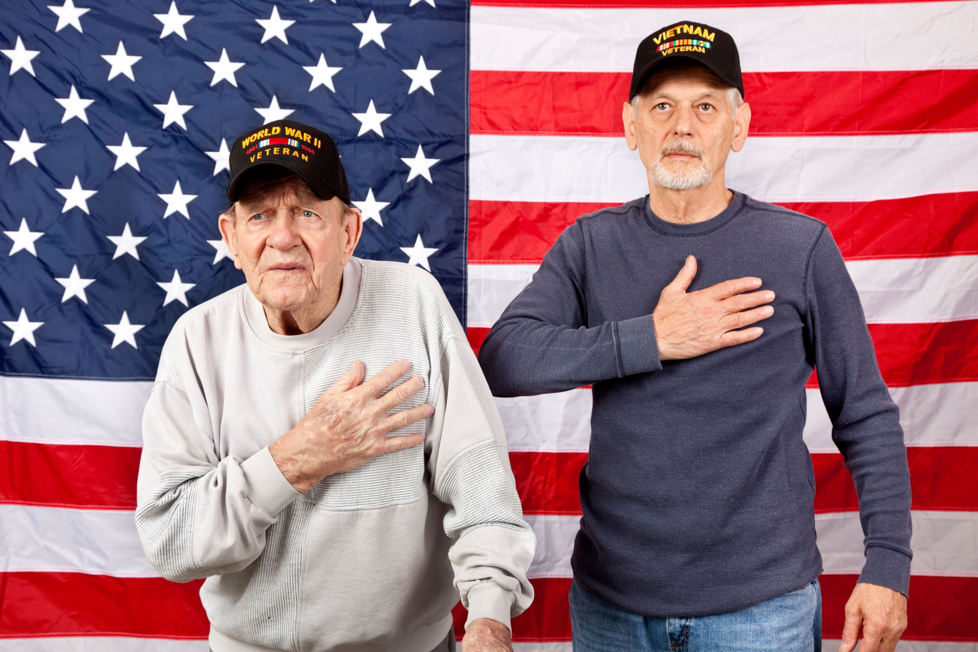Veterans standing in front of American Flag with hands over heart looking up
